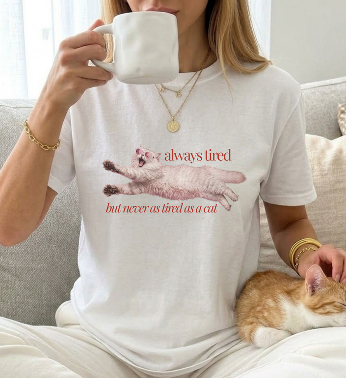 girl wearing a funny cat shirt with the quote always tired but never as tired as a cat drinking coffe and is cuddeling her cat