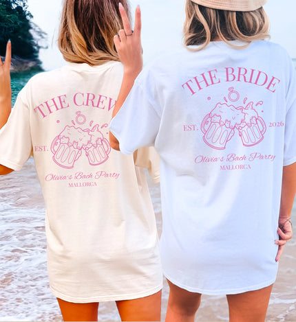 Zwei Frauen am Strand in personalisierten JGA Shirts von Cincerely Yours mit rosa Bierkrug-Motiv und 'The Bride' sowie 'The Crew' Aufdruck für den Junggesellinnenabschied.