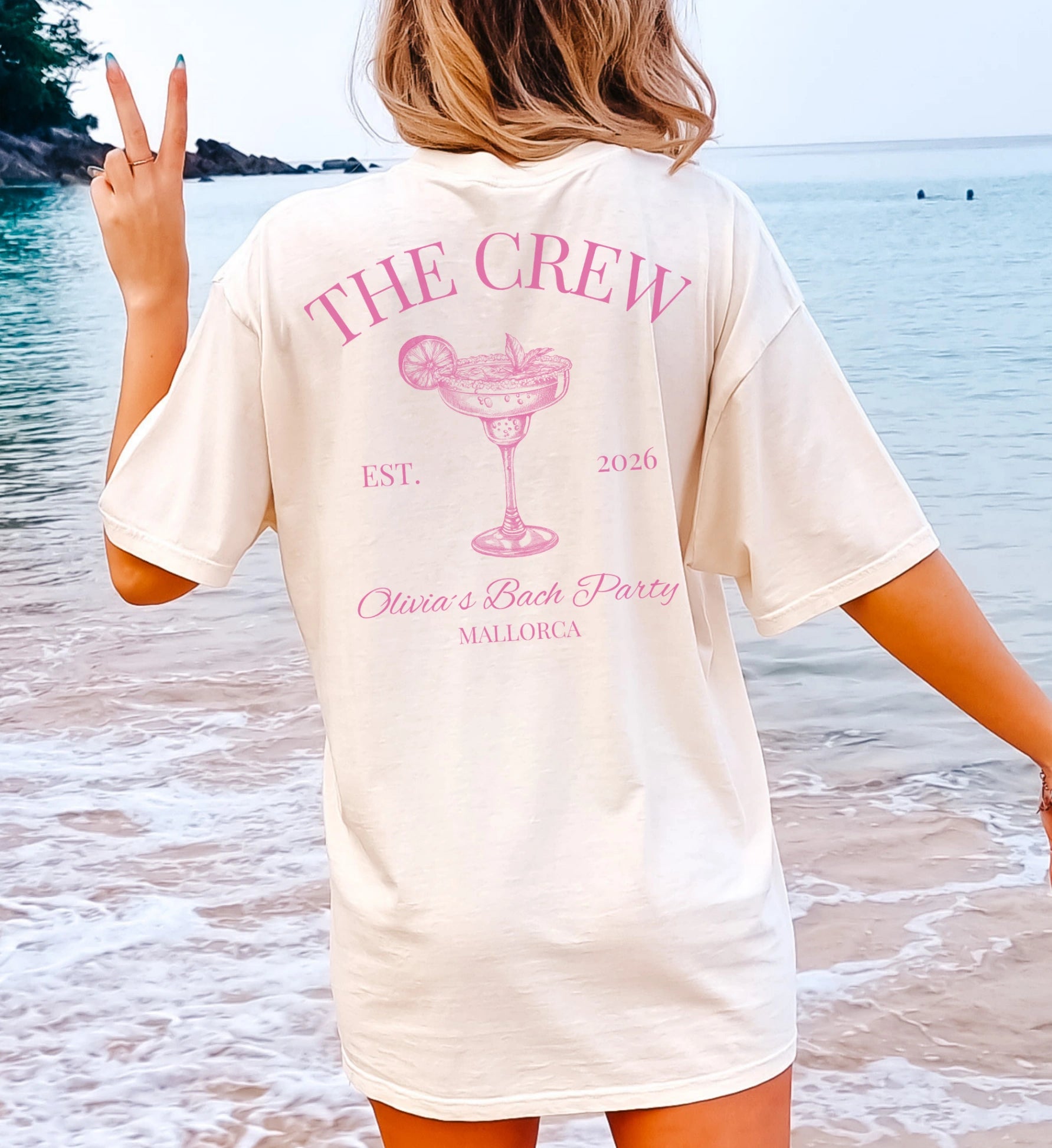 Beiges Oversized Bachelorette Shirt mit pinkem 'The Crew' Margarita-Print und Mallorca-Schriftzug, getragen von einer Frau am Strand für einen JGA.