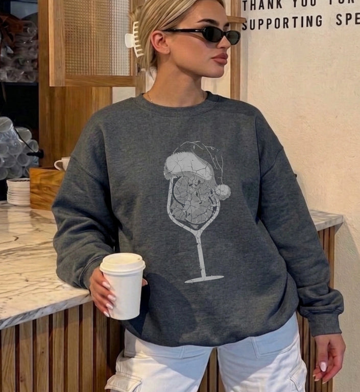 Eine junge Frau trägt einen dunkelgrauen bootleg Oversized Sweatshirt mit einem weißen Grafik-Print eines Spritz Cocktails mit Weihnachtsmütze im Bootleg-Stil.