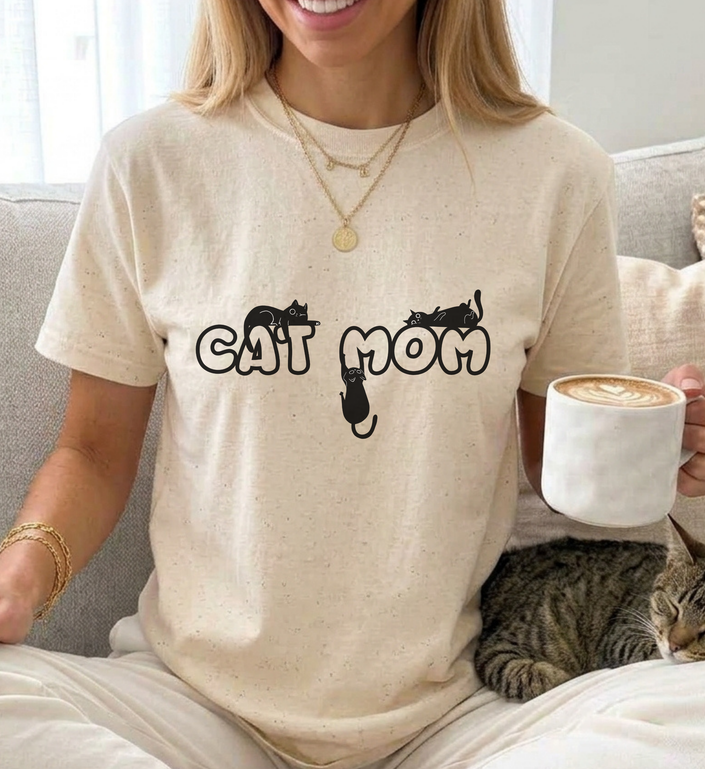 girl wearing a funny cat shirt with the quote cat mom with a cute cat design and bubble font, drinking coffe and is cuddeling her cat
