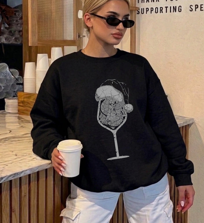 Eine Frau in einem schwarzen Centros Religious Sweatshirt, bedruckt mit einem künstlerischen, rissigen Spritz Cocktail Motiv und einer Weihnachtsmütze, lässig im Coffee-Shop.