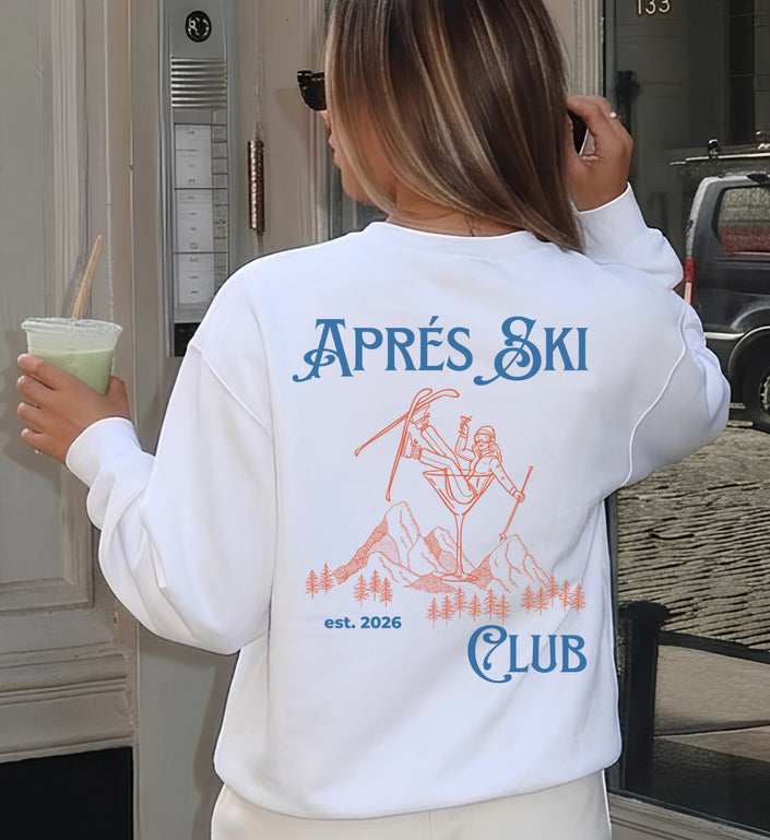 Rückenansicht eines weißen Cincerely Yours Sweatshirts mit blauem Aprés Ski Club Schriftzug und orangefarbenem Motivdruck einer Skifahrerin im Drink.