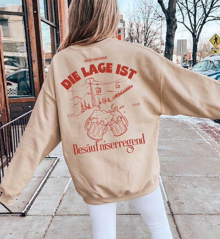 Rückansicht eines beigen Cincerely Yours Sweatshirts mit rotem Aprés Ski Print, Seilbahn und Bierkrug Grafik in einer urbanen Umgebung.