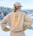 Rückenansicht eines beigen Sweatshirts mit großem Spritz-Cocktail-Motiv und dem Slogan Is always the answer vor einer verschneiten Winterlandschaft.
