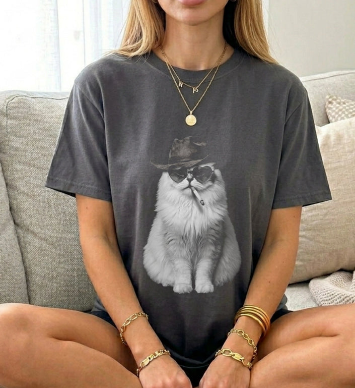 Frau im Schneidersitz trägt graues Oversize T-Shirt mit Print einer rauchenden Katze mit Cowboyhut und Herzbrille.