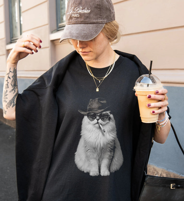 Streetwear Outfit mit schwarzem Oversized T-Shirt, cooler rauchender Katze als Frontprint, Basecap und Iced Coffee im urbanen Look.