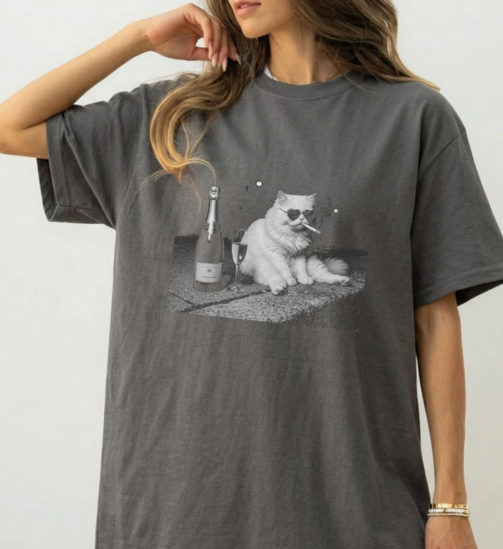 Nahaufnahme eines anthrazitfarbenen T-Shirts mit Grafikprint einer Katze im Bootleg-Stil, die eine Zigarette raucht und Champagner trinkt, lässiger Streetwear-Schnitt.