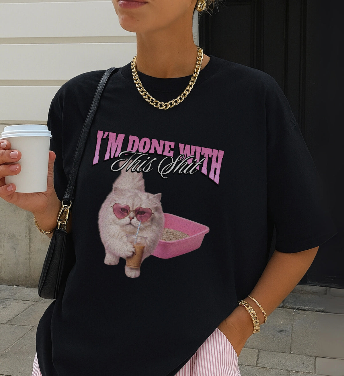 Schwarzes Cincerely Yours Oversized T-Shirt mit frechem Katzen-Design, Herzbrille und Kaffee, modisch gestylt mit goldener Kette und Streifenshorts.
