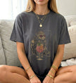 Nahaufnahme einer Frau in einem grauen T-Shirt mit einer illustrierten, gekrönten Katze, die eine herzförmige Sonnenbrille trägt und neben einem erfrischenden sommerlichen Spritz-Cocktail sitzt.