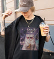 Stylische Frau mit Kappe trägt ein schwarzes T-Shirt mit Cat-Disco-Palmen Grafik, hält einen Iced Coffee in der Hand, urbaner Streetstyle Look.