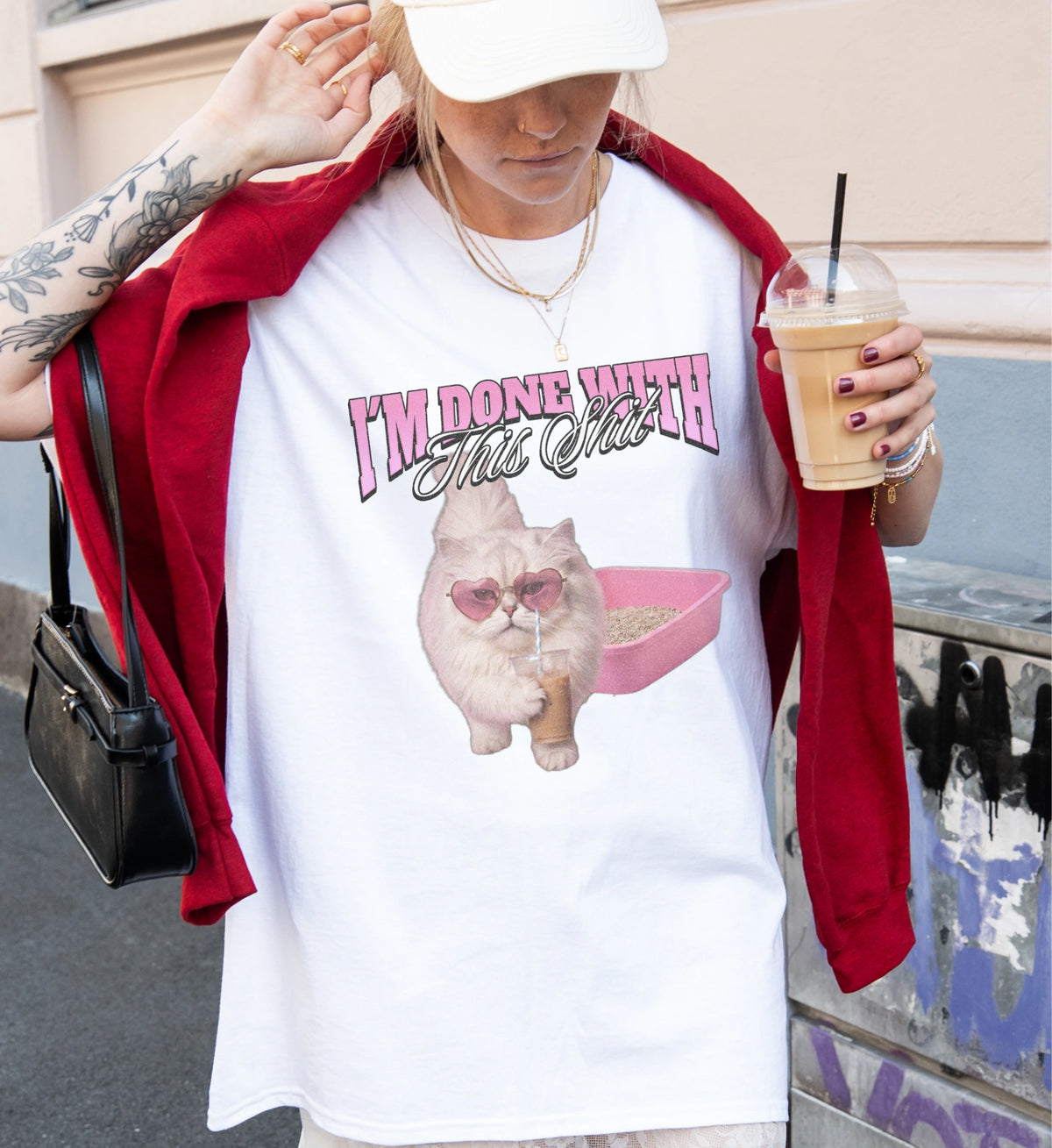 Weißes Cincerely Yours T-Shirt im Bootleg-Stil mit Grafik einer flauschigen Katze mit Herzsonnenbrille, Kaffeebecher und Katzentoilette, getragen zu rotem Sweatshirt.