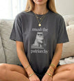 Stylische Frau trägt ein anthrazitfarbenes Vintage-T-Shirt mit einem Cat-Motiv, das eine Sonnenbrille trägt und eine Tasse hält, im Sitzen fotografiert.