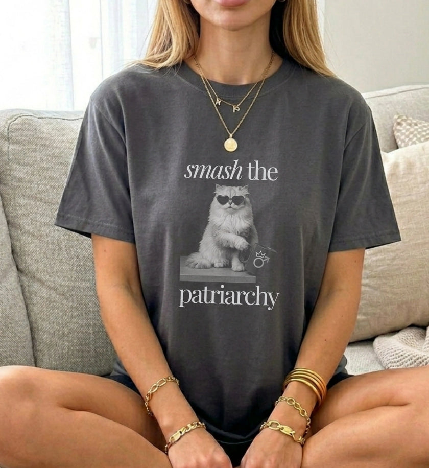 Stylische Frau trägt ein anthrazitfarbenes Vintage-T-Shirt mit einem Cat-Motiv, das eine Sonnenbrille trägt und eine Tasse hält, im Sitzen fotografiert.