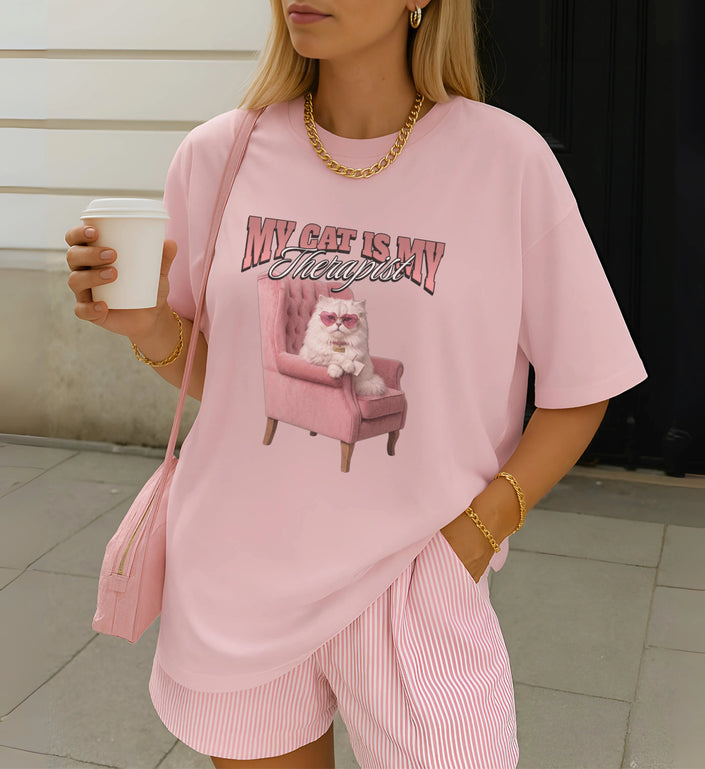 Hellrosa Cincerely Yours T-Shirt mit unhinged Katzen-Print, Herzbrille und Sessel. Der Stil ist Y2K inspiriert, präsentiert in einem casual Street-Style.