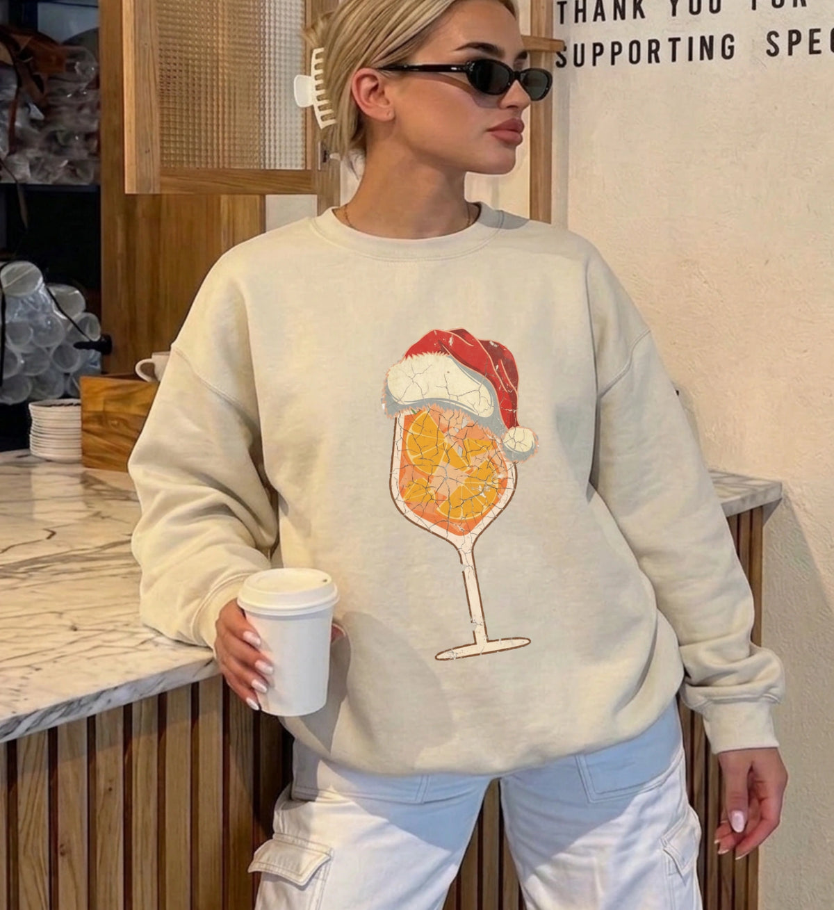 Cremefarbener Christmas Sweater von Cincerely Yours mit detailreichem Spritz-Cocktail Motiv im Used-Look mit Weihnachtsmütze, ideal als Outfit für Firmen-Weihnachtsfeiern.
