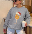 Frau trägt einen grauen Cincerely Yours Christmas Sweater mit aufgedrucktem Spritz-Cocktail Glas, das eine Weihnachtsmütze trägt, Vintage-Grafik-Stil, lässiger Oversize-Schnitt.