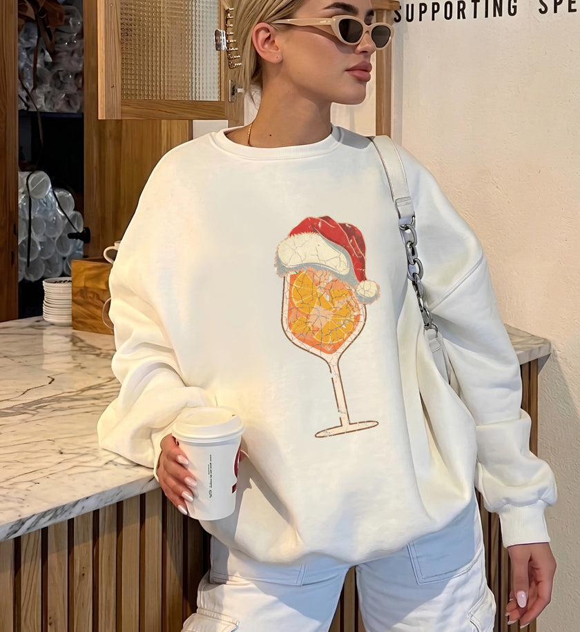 Weißes Langarm-Sweatshirt der Marke Cincerely Yours mit weihnachtlichem Cocktail-Print, trägt Weihnachtsmannmütze, perfekt kombiniert zu heller Hose für einen modernen Party-Look.