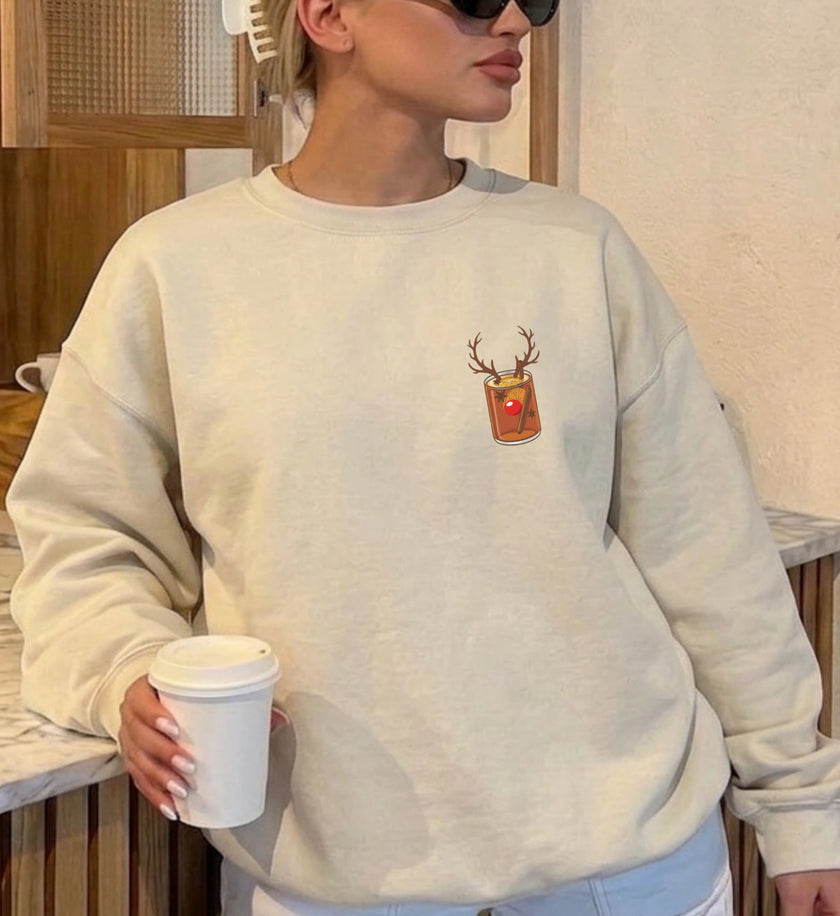 Vorderansicht eines beigen Oversized Sweatshirts mit einem dezenten, kleinen Brustaufdruck, der eine Glühweintasse mit Rentiergeweih und roter Nase darstellt, im Innenraum.