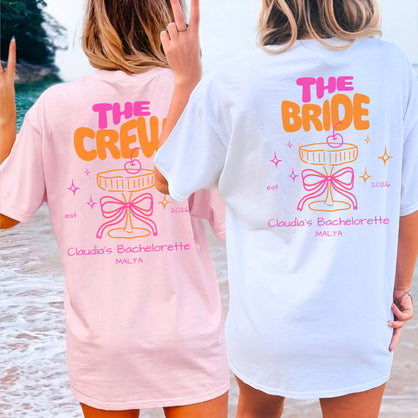 Zwei Frauen am Strand in personalisierten Coquette Bachelorette Shirts von Cincerely Yours: Rosa 'The Crew' und weißes 'The Bride' T-Shirt mit Neon-Cocktail-Design, Schleife und JGA-Aufdruck in der Rückansicht.