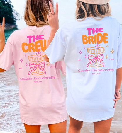 Zwei Frauen am Strand in personalisierten Coquette Bachelorette Shirts von Cincerely Yours: Rosa 'The Crew' und weißes 'The Bride' T-Shirt mit Neon-Cocktail-Design, Schleife und JGA-Aufdruck in der Rückansicht.