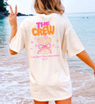 Beiges Cincerely Yours Coquette Bachelorette Shirt mit Neon 'The Crew' Print, Cocktail-Grafik und pinker Schleife für den JGA, getragen am Strand in der Rückansicht.
