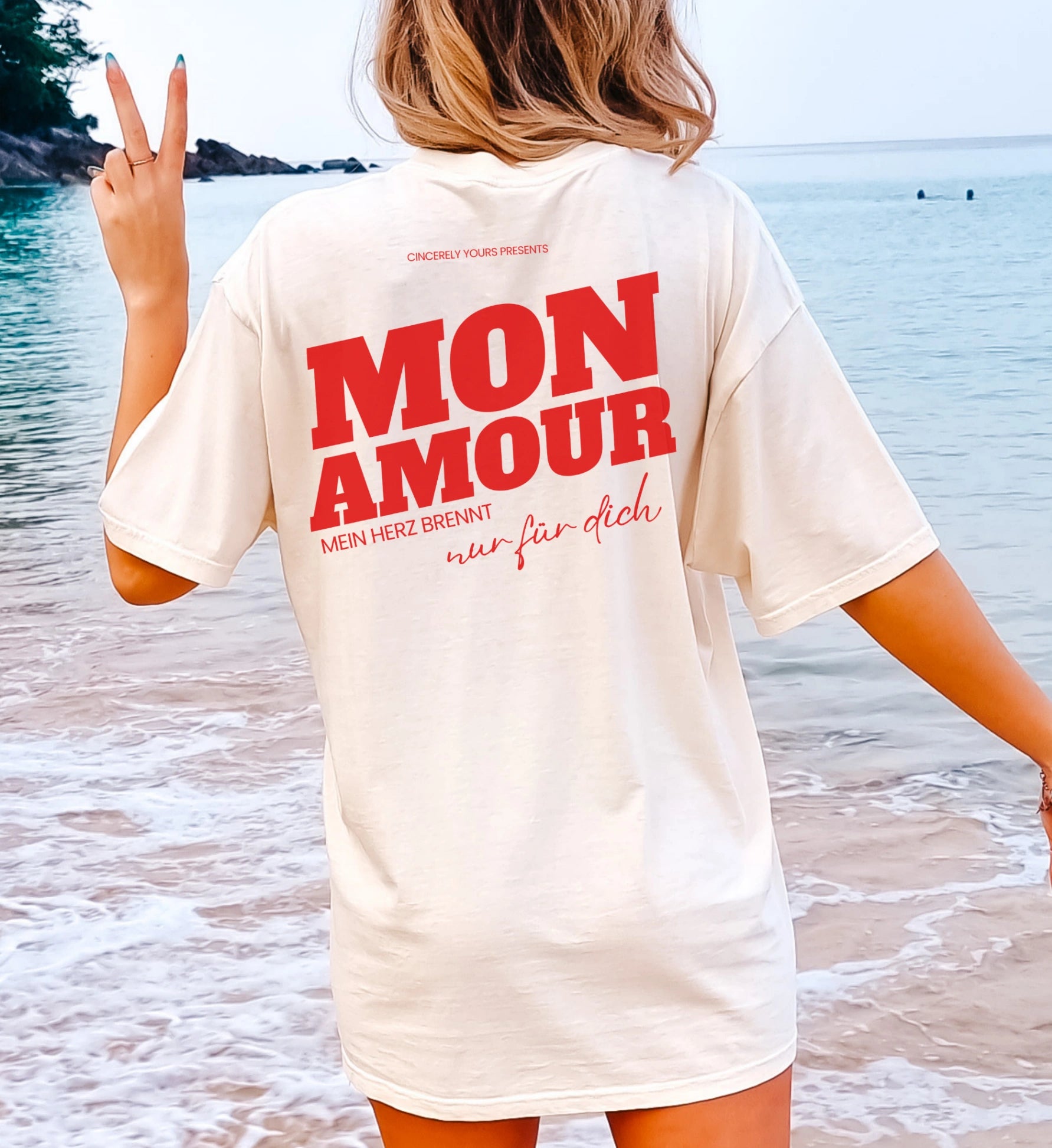 Cincerely Yours Malle Party Shirt in Cremeweiß mit rotem 'Mon Amour' Backprint und Spruch 'Mein Herz brennt nur für dich', Rückansicht einer Frau am Strand.