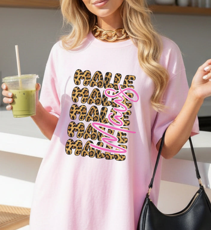 Eine Frau trägt ein rosa T-Shirt mit Mallemaus Motiv in Leopardmuster und pinkem Bubble-Schriftzug, kombiniert mit einer schwarzen Handtasche.