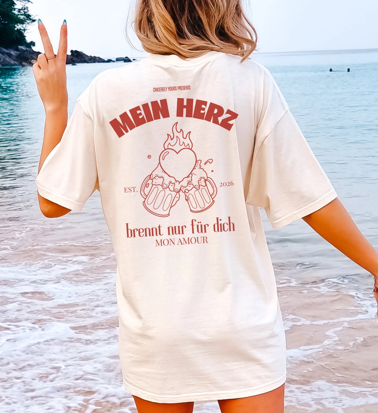 Cincerely Yours Oversize T-Shirt in Creme mit Rückenprint 'Mein Herz brennt nur für dich' und Illustration von anstoßenden Bierkrügen mit Herzflamme, getragen am Strand.