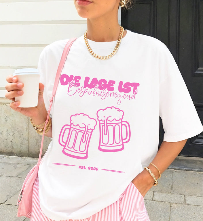 Ein weißes Party T-Shirt mit pinkem Aufdruck Die Lage ist besäufniserregend und Bierkrug-Grafik, kombiniert mit einer rosafarbenen Tasche und goldenem Schmuck.