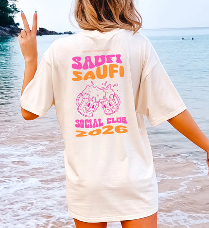 Frau am Strand trägt ein weißes Oversize Party Shirt von Cincerely Yours mit dem Backprint Saufi Saufi Social Club 2026 und zwei lachenden Bierkrügen.