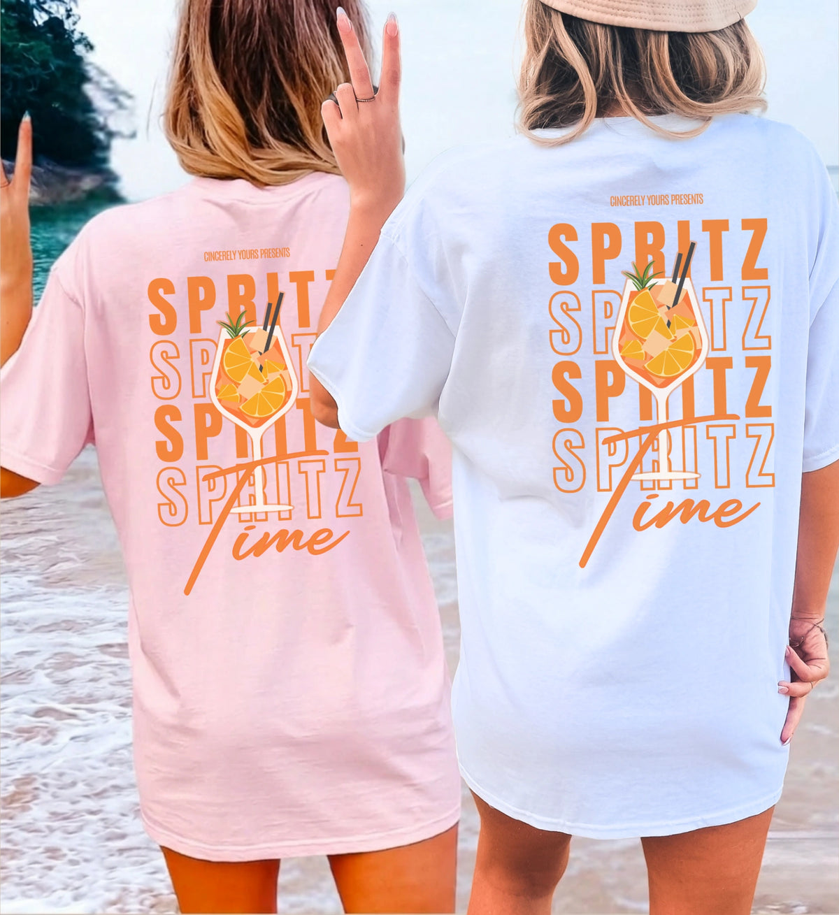 Zwei Frauen in hellen T-Shirts mit orangefarbenem Spritz Time Backprint, stehend am Strand mit Blick auf das Meer, sommerliche Urlaubsstimmung.