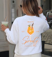 Rückenansicht eines weißen Sweatshirts mit farbenfrohem Cocktail-Grafikdruck, der einen italienischen Aperitif zeigt, kombiniert mit lässigem Alltagsoutfit.