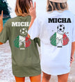 Zwei Personen am Strand tragen personalisierte T-Shirts für Italien-Fans mit einem Motiv aus anstoßenden Bierkrügen in den Nationalfarben Grün, Weiß und Rot, einem Fußball und dem Namen Micha sowie der Jahreszahl 2026.