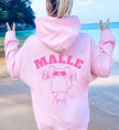 Hellrosa Oversized Hoodie mit Malle Maus Print auf der Rückseite, getragen von einer Frau am Strand mit Blick auf das türkisfarbene Meer.
