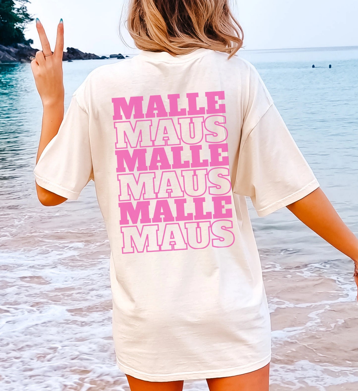 Oversized T-Shirt in Cremeweiß mit pinkem Malle Maus Rückenprint, getragen von einer Frau am Strand mit Peace-Zeichen.
