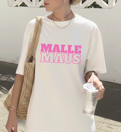 Frau trägt ein weißes Oversized T-Shirt mit dem pinken Aufdruck Malle Maus, kombiniert mit Goldschmuck und einer sommerlichen Korbtasche.