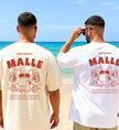 Zwei Männer am Strand in T-Shirts für den Malle-Urlaub mit einem witzigen Grafik-Design auf dem Rücken. Das Motiv zeigt eine Maus mit Sonnenbrille in einem Flamingo-Schwimmreifen, die zwei Bierkrüge hält, ergänzt durch den Spruch: Eigentlich sind wir doch zum Saufen da.