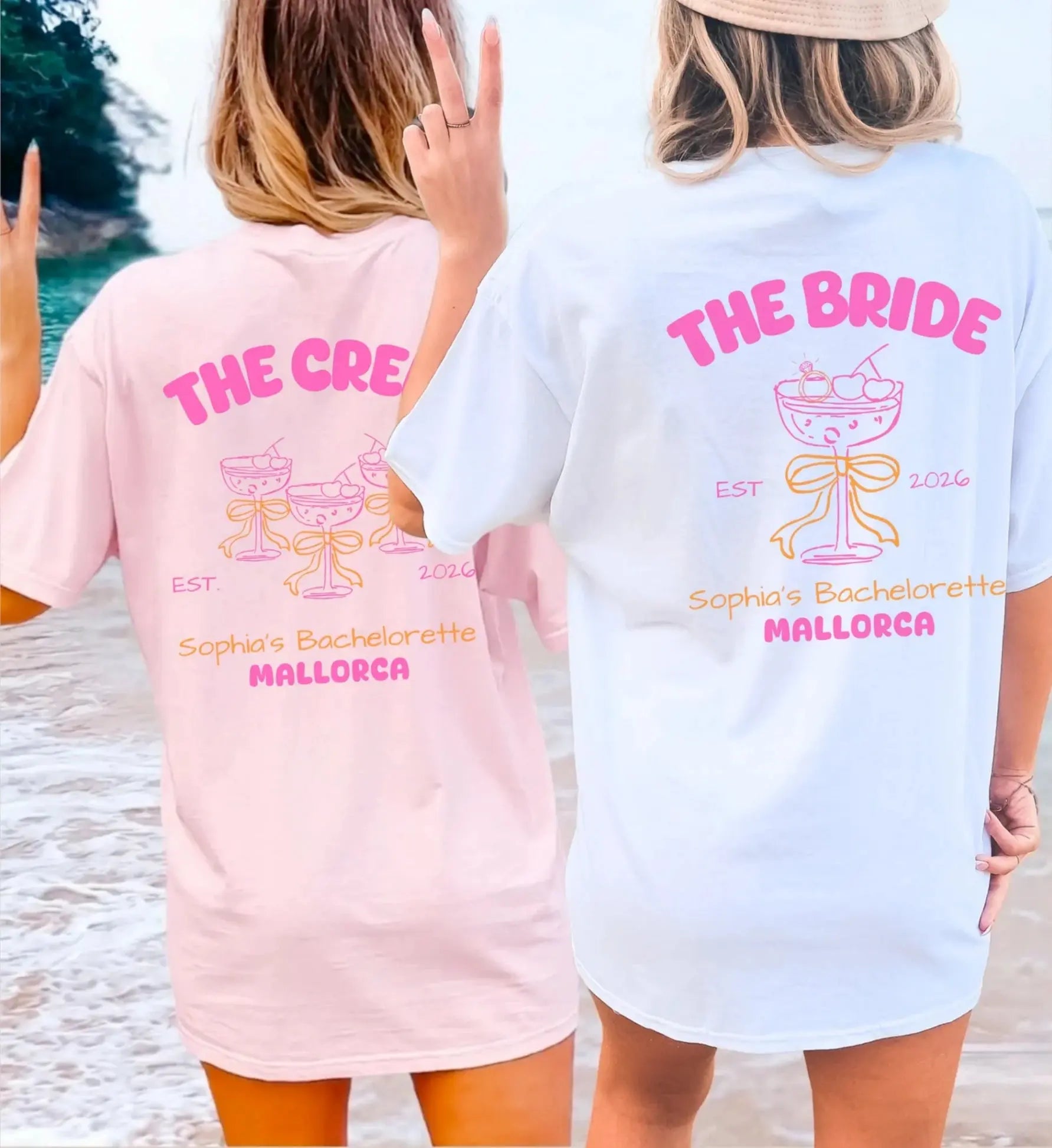 Zwei Frauen am Strand in personalisierten JGA-Shirts für die Braut und die Crew, hellrosa und weiß, mit Coquette-Design, Schleifen und Champagnerglas-Illustration für einen Junggesellinnenabschied auf Mallorca.