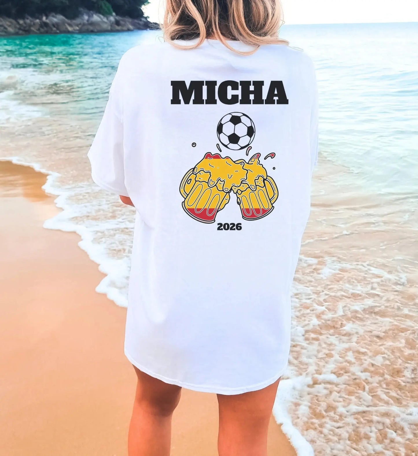 Personalisierbares weißes T-Shirt mit dem Namen Micha, einem Fußball-Motiv und anstoßenden Bierkrügen in spanischen Farben vor einer Strandkulisse.