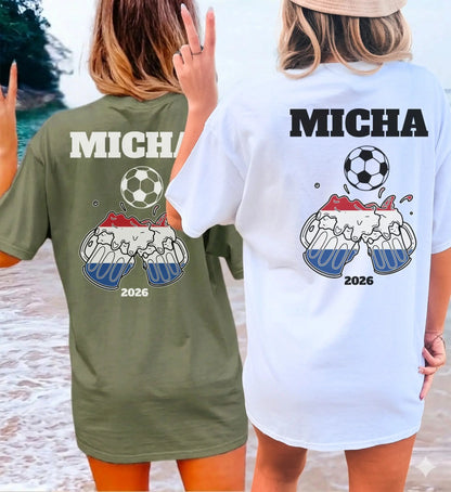Zwei Frauen am Strand tragen personalisierte T-Shirts für niederländische Fußballfans mit Namen, Fußball-Motiv und anstoßenden Bierkrügen in den Landesfarben für den Gruppenurlaub.