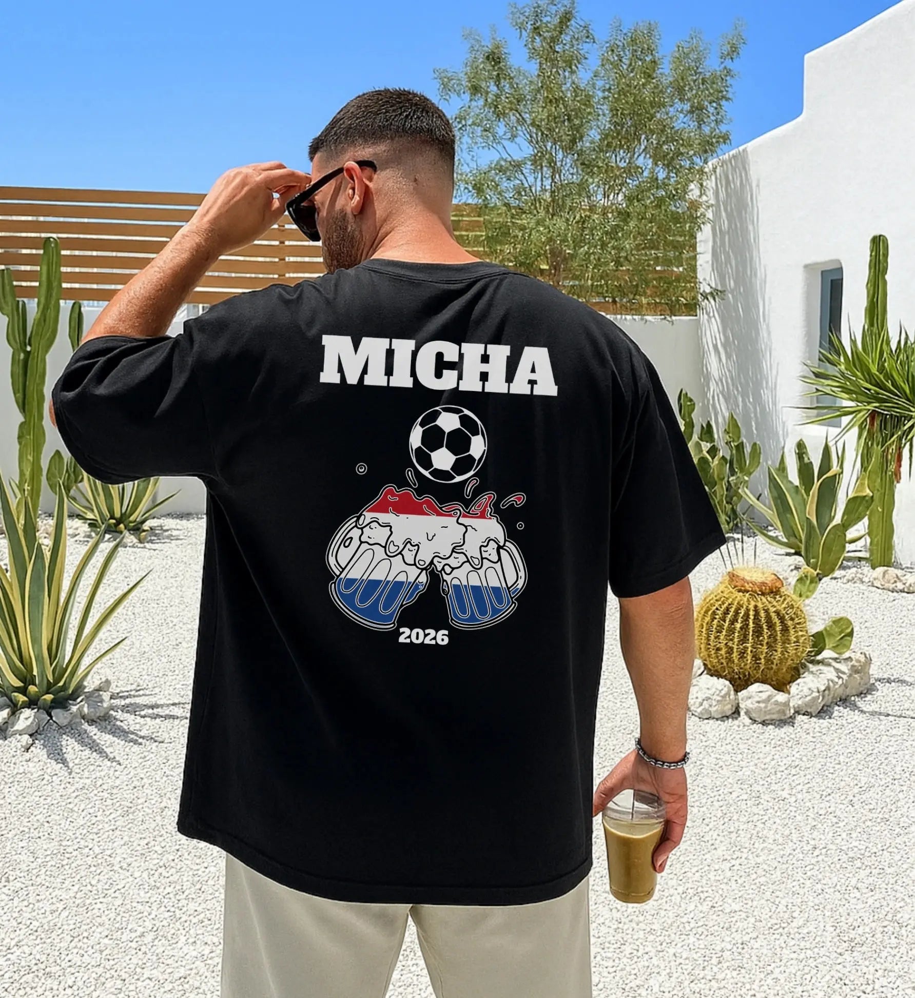 Mann von hinten in einem schwarzen Oversized T-Shirt mit dem Namen Micha, einem Fußball und Bierkrügen in den Farben der niederländischen Flagge für den Urlaub 2026.