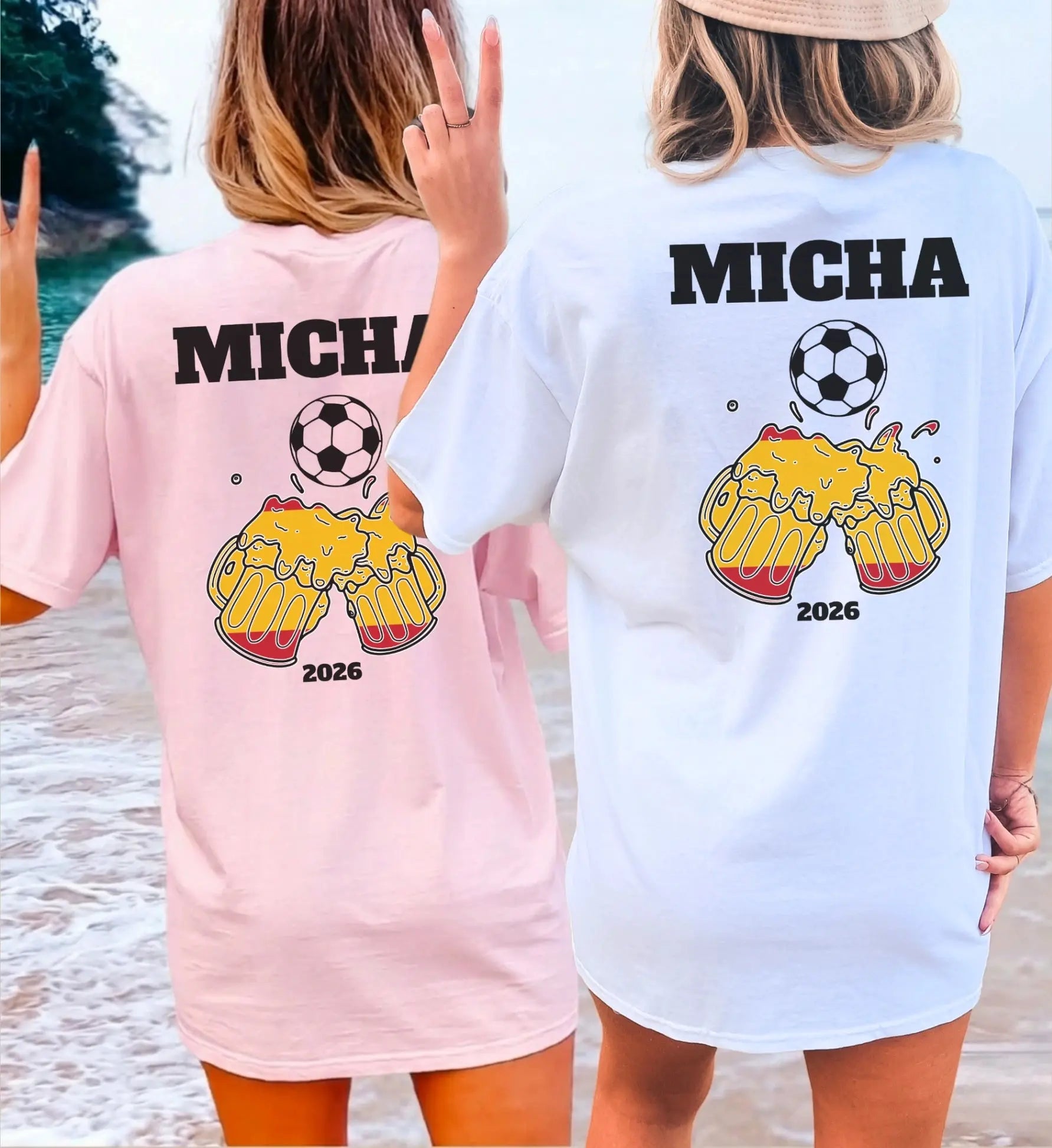 Zwei Frauen am Strand in personalisierten Oversize-T-Shirts in Rosa und Weiß mit Fußball-Motiv, anstoßenden Bierkrügen in Spanien-Farben und dem Namen Micha für den Mallorca Urlaub 2026.