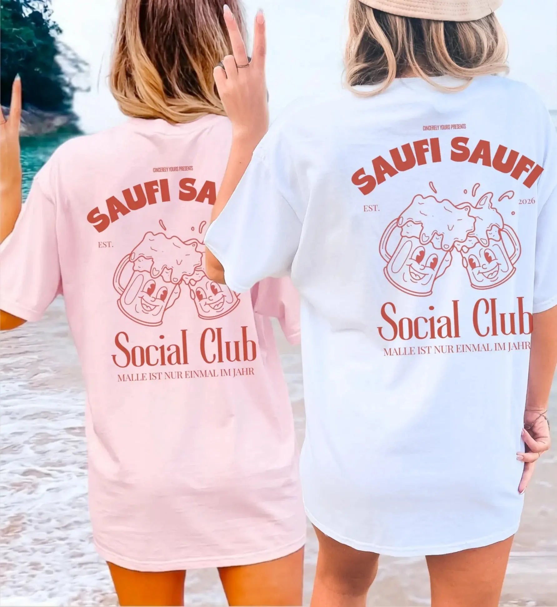 Zwei Frauen am Strand in oversized T-Shirts (Rosa und Weiß) mit Saufi Saufi Social Club Rückenprint und lachenden Bierkrug-Maskottchen.