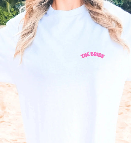 Weißes Damen T-Shirt mit neon-pinkem 'THE BRIDE' Schriftzug auf der Brust, ideal für den Junggesellinnenabschied am Strand.